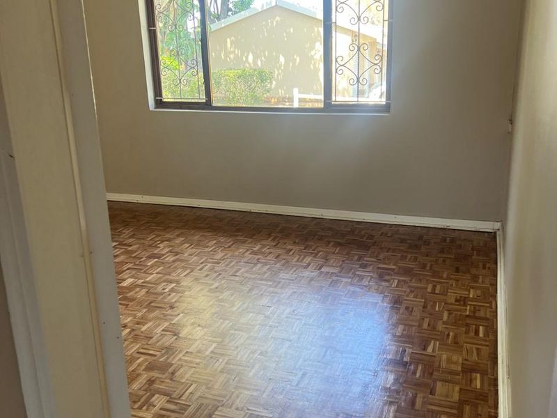 A vacant bedroom featuring classic parquet flooring, neutral wall tones, and a window fitted with security bars.