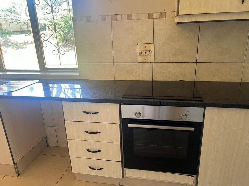 Functional kitchen featuring granite countertops, built-in oven, electric hob, and tiled backsplash with ample storage cabinetry.