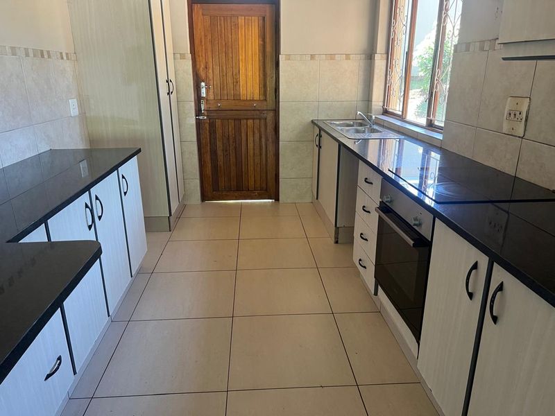 A functional kitchen featuring granite countertops, built-in oven and hob, tiled flooring, and ample cabinetry, providing a clean and practical workspace.