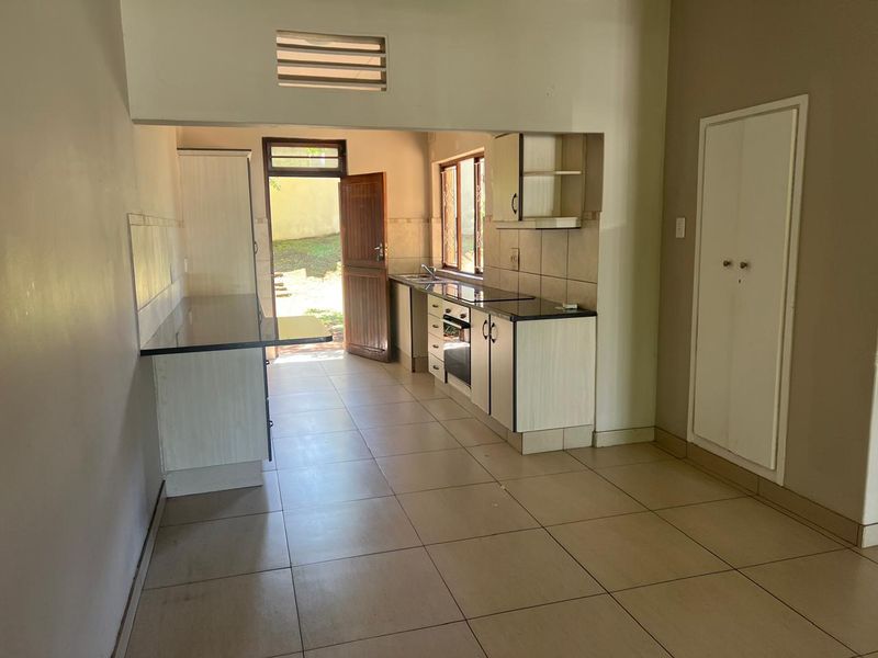 A functional kitchen featuring built-in cabinetry, granite countertops, an integrated oven and hob, and direct access to the rear exterior.