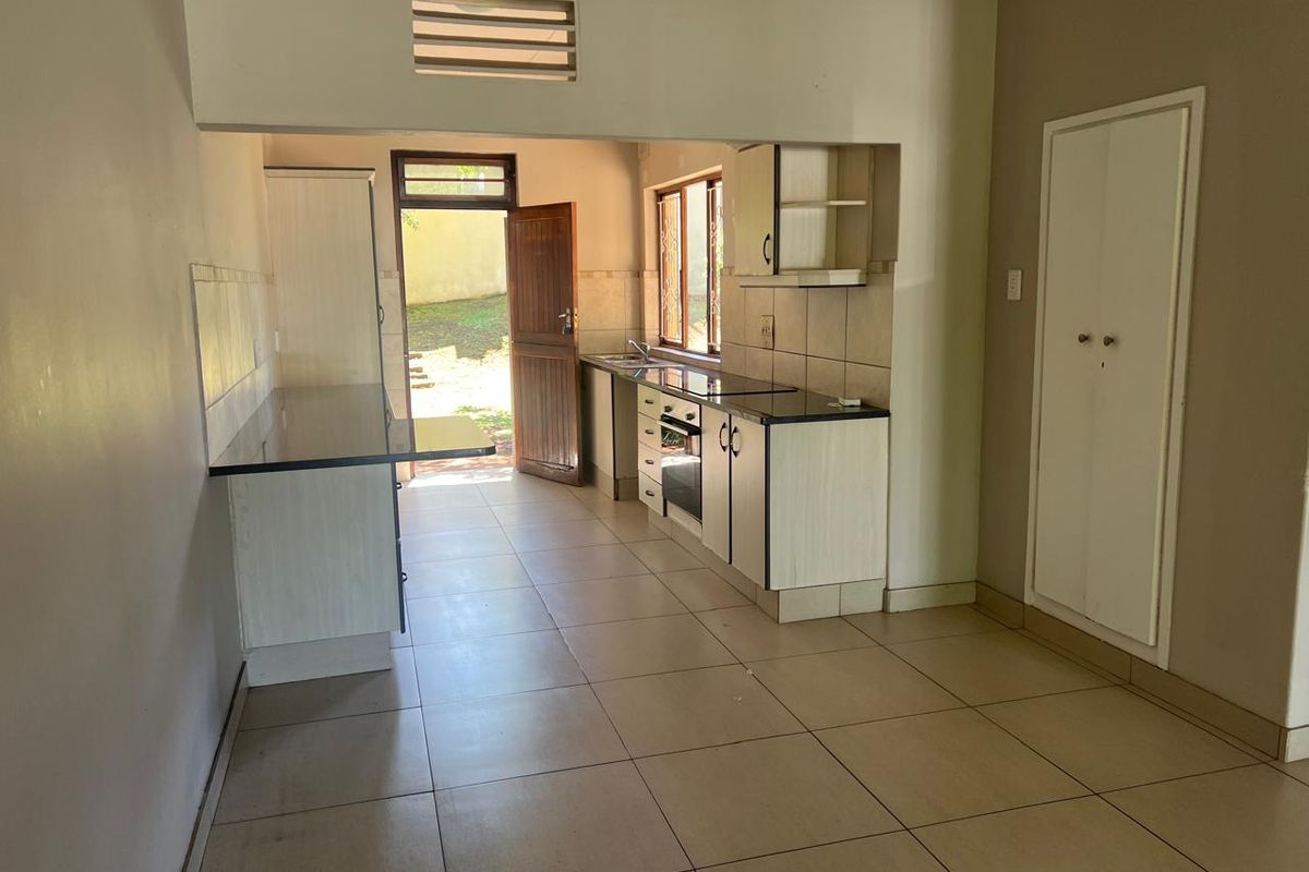 A functional kitchen featuring built-in cabinetry, granite countertops, an integrated oven and hob, and direct access to the rear exterior.