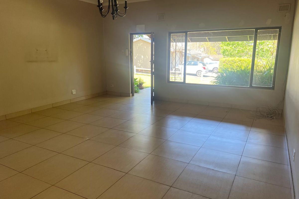 A spacious, empty living room featuring neutral tiled flooring, a large window with security bars, and direct access to the exterior.