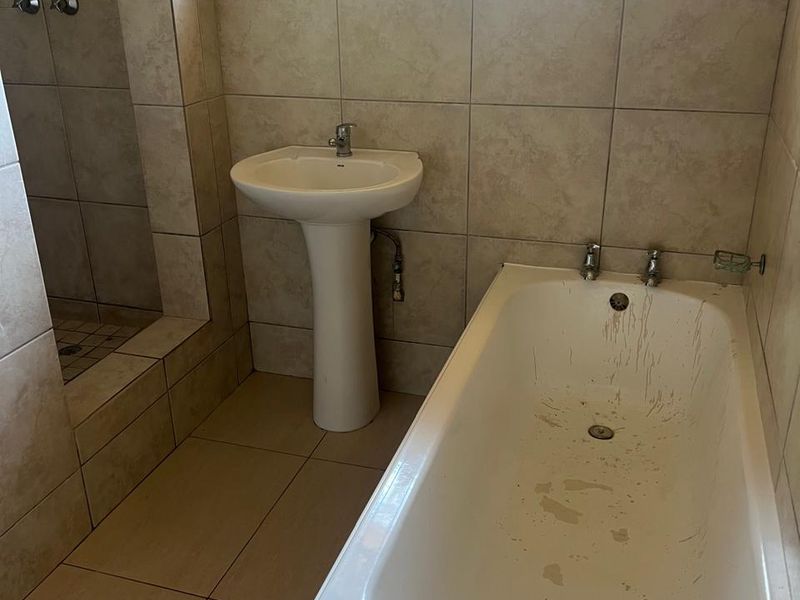 A functional bathroom featuring a pedestal basin, built-in bathtub, and a walk-in shower with tiled finishes and security bars on the window.