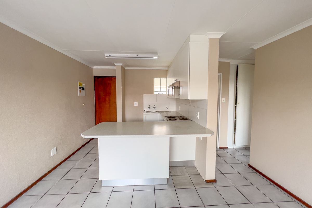 A functional, open-plan kitchen featuring white built-in cabinetry, a laminate breakfast bar, electric hob, and tiled flooring throughout.