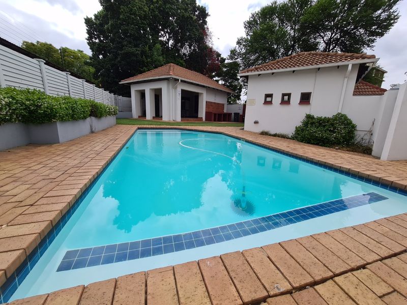 A well-maintained outdoor pool area featuring brick paving, a clear swimming pool, and adjacent covered patio structure with tiled roofing.
