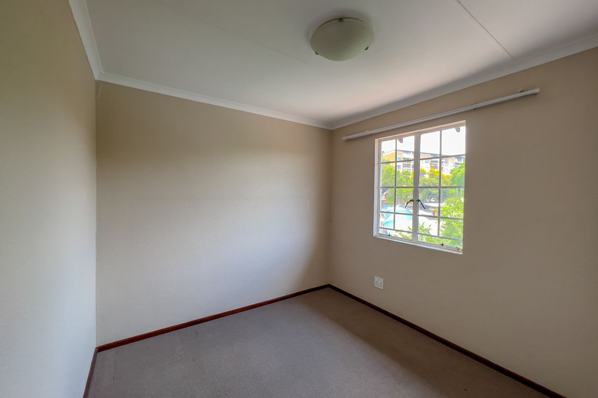 An empty bedroom featuring neutral walls, carpet flooring, and a window providing natural light.