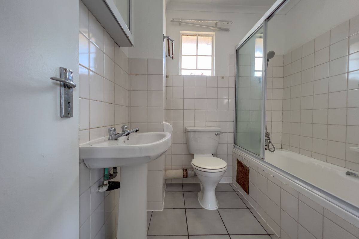 A functional bathroom featuring a pedestal basin, toilet, and a bathtub with a shower screen, finished with white wall tiles and floor tiles.