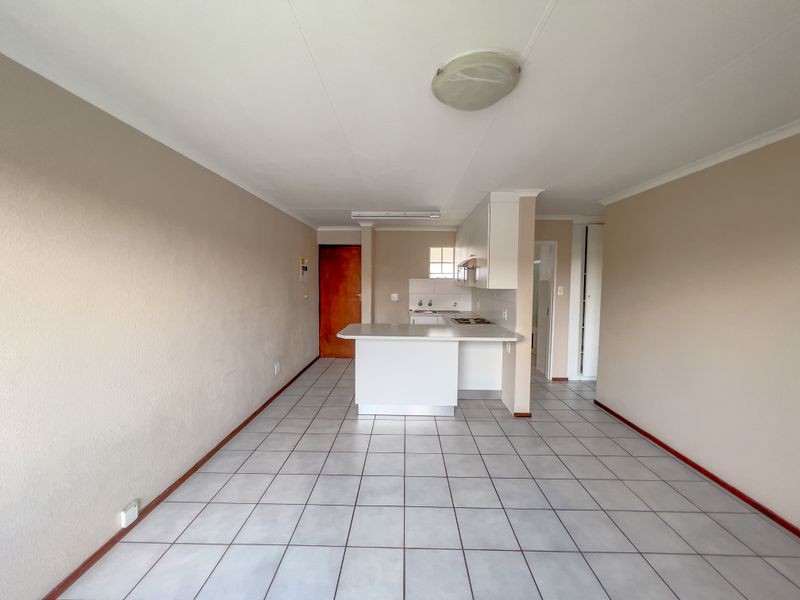 An open-plan living and kitchen area featuring tiled flooring, a breakfast bar, and built-in kitchen appliances in a neutral, vacant space.