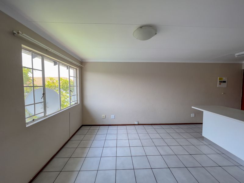 An empty open-plan living area featuring neutral tiled flooring, a breakfast counter, and large windows providing natural light.
