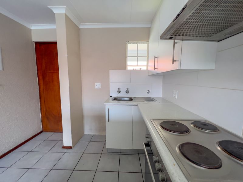 A functional kitchen featuring white cabinetry, a stainless steel sink, built-in electric hob and oven, and tiled flooring.