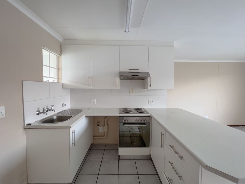 A clean, functional kitchen featuring white cabinetry, a breakfast bar, tiled flooring, and integrated appliances including an oven, hob, and extractor fan.