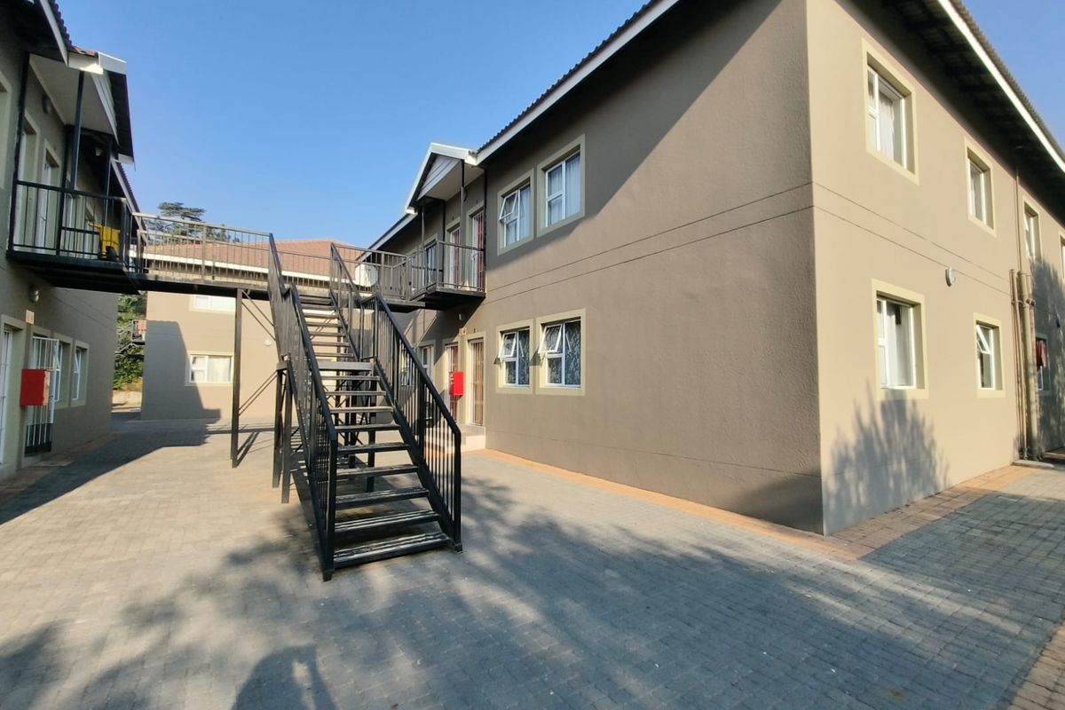Exterior view of an apartment complex featuring a paved courtyard, metal staircase, and elevated walkway connecting the building units.
