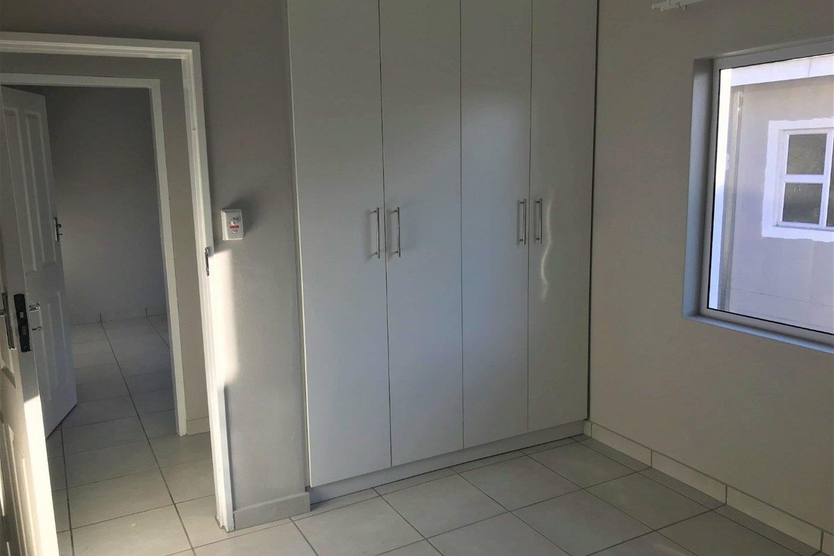 A clean, empty bedroom featuring neutral tiled flooring, built-in cupboards, and a window providing natural light.