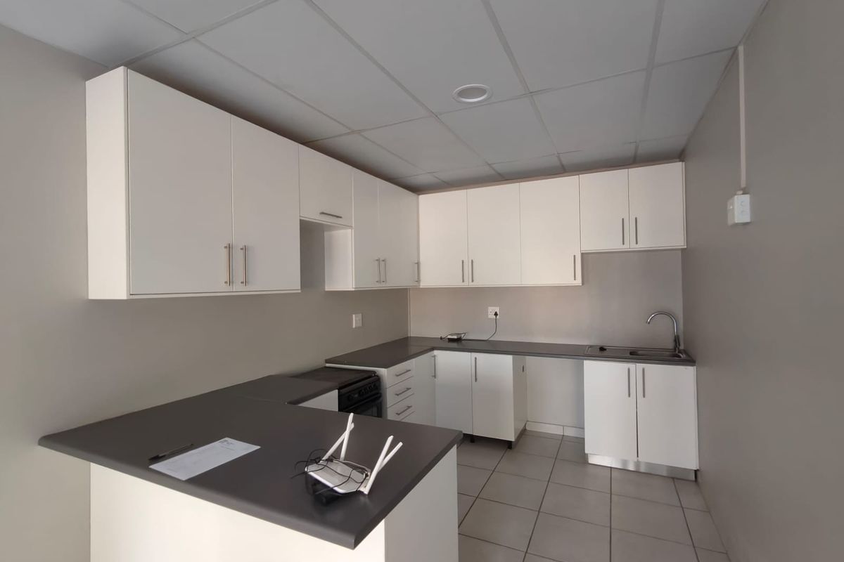 A clean, functional kitchen featuring white cabinetry, dark laminate countertops, a stainless steel sink, and tiled flooring in a neutral, well-lit space.