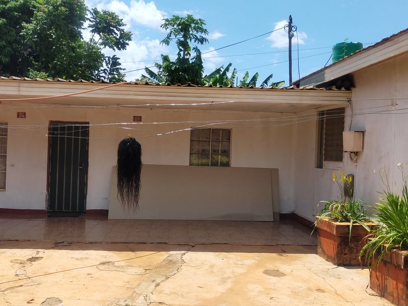 A covered outdoor patio area featuring tiled flooring, brick planter boxes, and direct access to the home via a security gate.