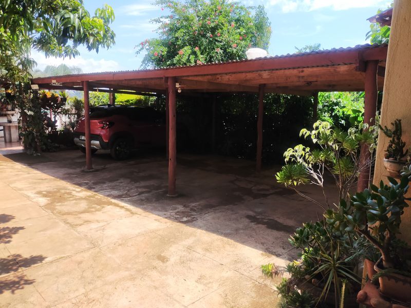 A covered outdoor parking area featuring a timber post structure with a corrugated roof and concrete paving.