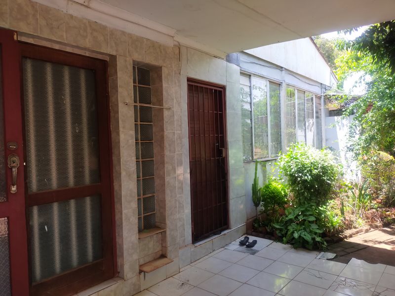 A covered patio area featuring tiled flooring, a glass block feature wall, and direct access to the garden through security-gated doors.