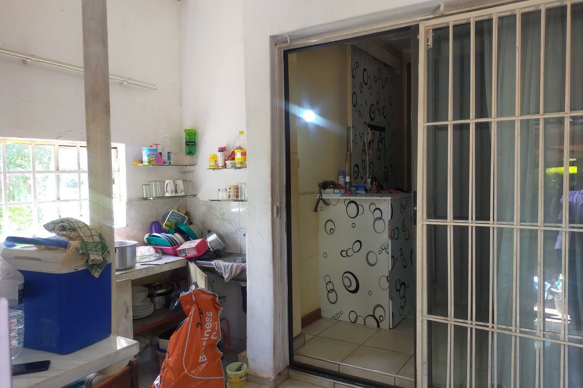 A functional kitchen area featuring tiled flooring, a stainless steel sink, and direct access to an adjacent space through a sliding security door.