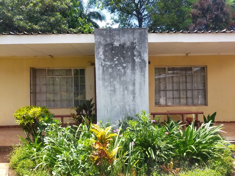 Front exterior view of the apartment building featuring metal-framed windows and a central concrete pillar requiring maintenance and cosmetic updates.