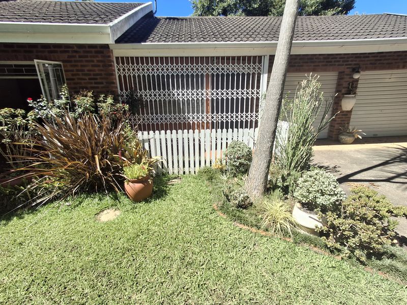 Front exterior view of a townhouse featuring a brick facade, tiled roof, security gate, and a small garden area with a concrete driveway.