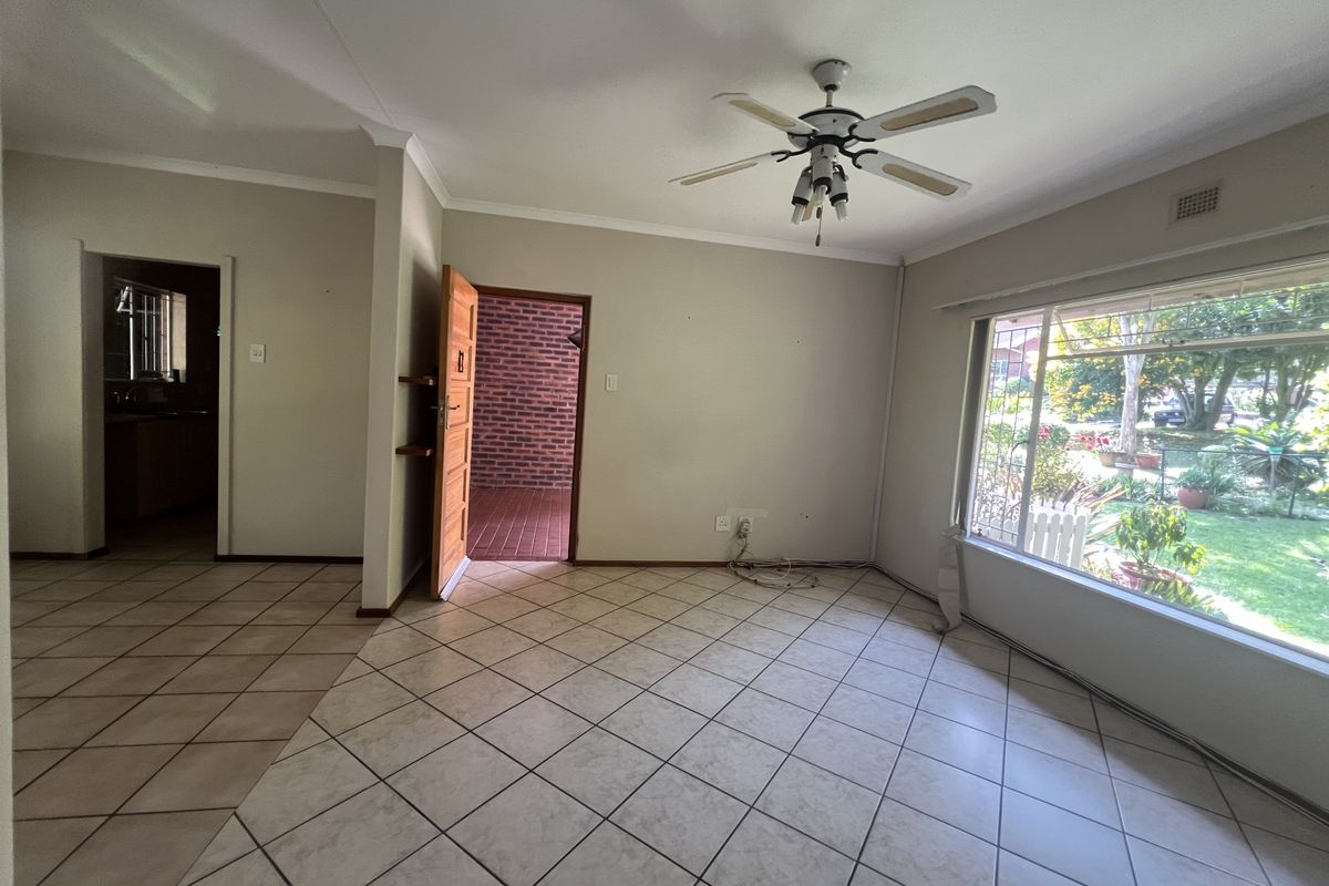 An empty living room featuring ceramic floor tiles, a ceiling fan, and a large window overlooking the garden.