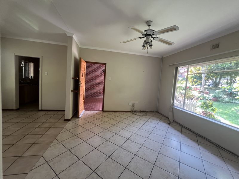 An empty living room featuring ceramic floor tiles, a ceiling fan, and a large window overlooking the garden.