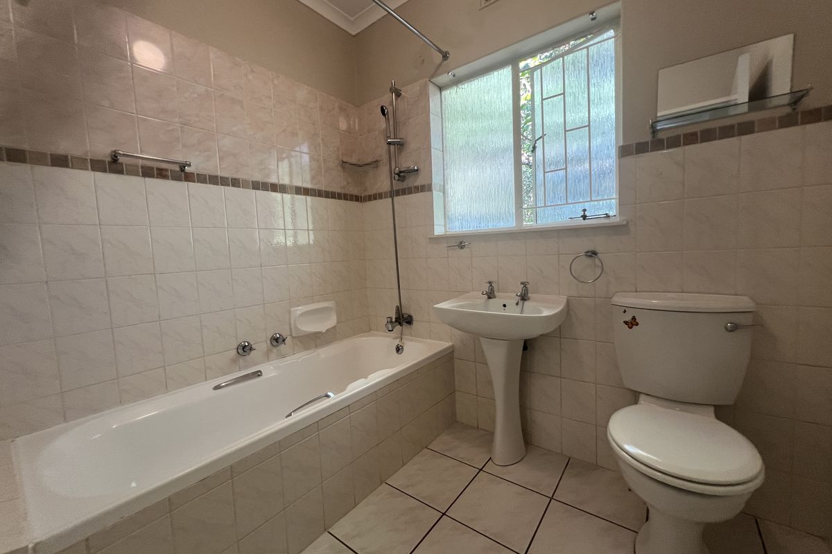 A functional bathroom featuring a bathtub, pedestal basin, and toilet with neutral wall and floor tiling, offering a clean and practical layout.