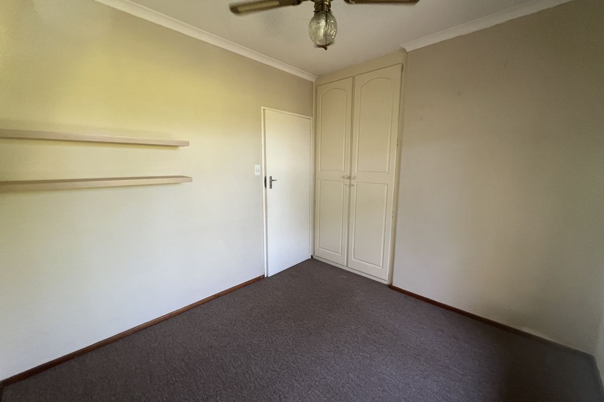 A vacant bedroom featuring neutral walls, carpeted flooring, built-in cupboards, and a ceiling fan, offering a clean canvas for personalization.