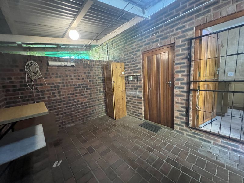 A covered outdoor patio area featuring exposed brick walls, paved flooring, and direct access to the interior through a timber door with a security gate.