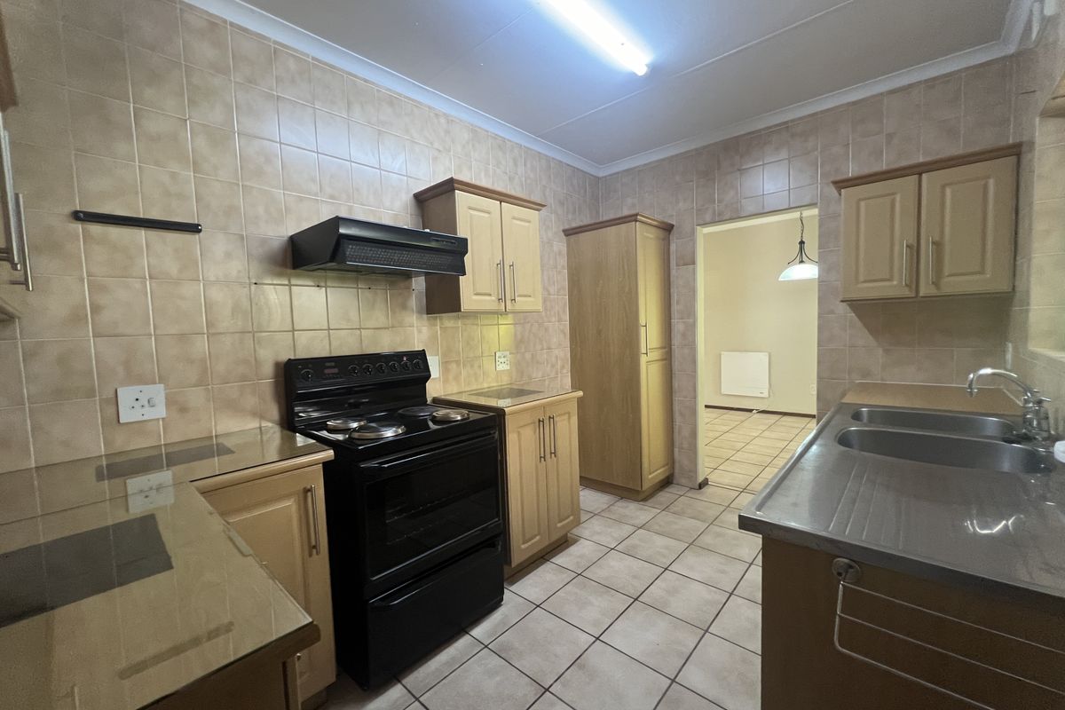 A functional kitchen featuring wooden cabinetry, tiled splashbacks, a stainless steel sink, and a freestanding stove with an extractor fan.