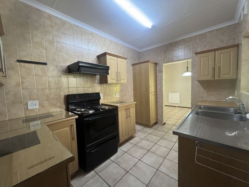 A functional kitchen featuring wooden cabinetry, tiled splashbacks, a stainless steel sink, and a freestanding stove with an extractor fan.