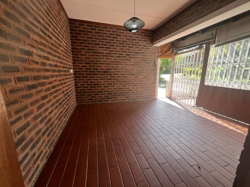 A covered patio area featuring exposed brick walls, tiled flooring, and a secure metal gate entrance.