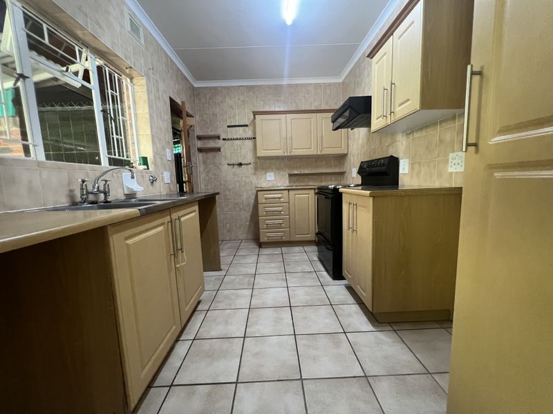 A functional kitchen featuring light wood-tone cabinetry, tiled splashbacks, ceramic flooring, and built-in appliances, offering a practical layout with ample storage space.