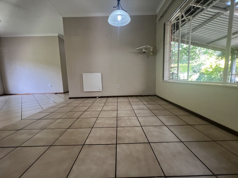 An empty living area featuring ceramic floor tiles, a wall-mounted electric heater, and large windows with security bars, offering a blank canvas for interior design.