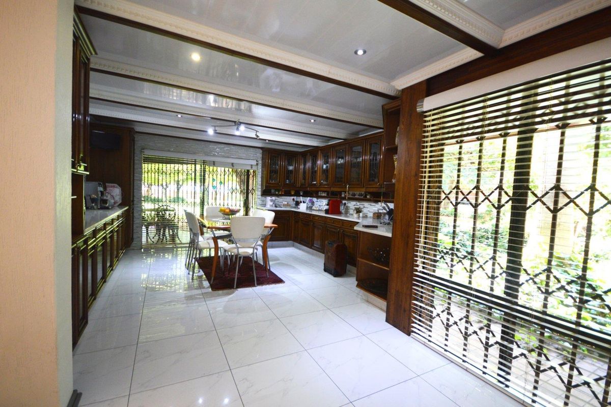 Spacious kitchen featuring extensive wooden cabinetry, stone countertops, tiled flooring, and large windows with security gates, offering a functional and well-lit cooking and dining area.