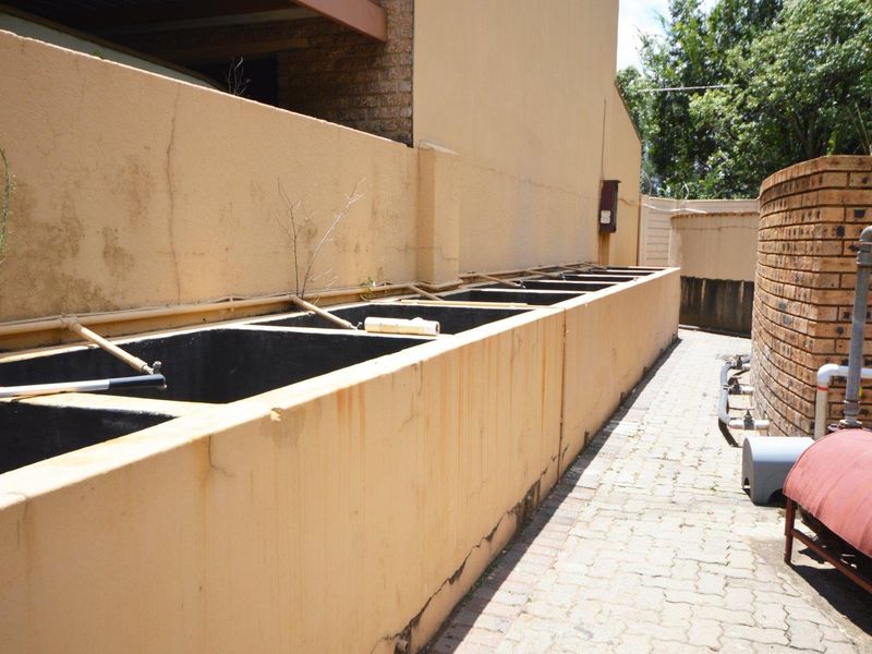 Exterior utility area featuring a series of concrete troughs, brick masonry walls, and a paved walkway with visible external plumbing infrastructure.