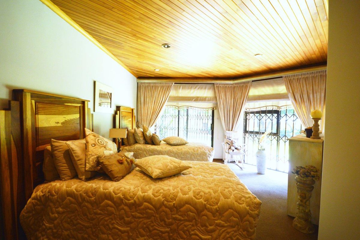 Spacious bedroom featuring a warm timber tongue and groove ceiling, recessed lighting, and large windows with integrated security gates.
