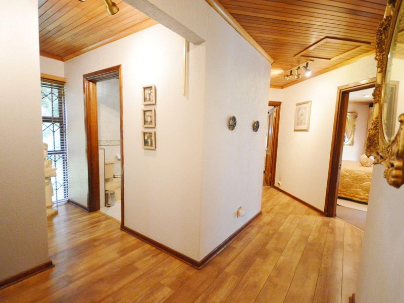 A well-maintained hallway featuring warm timber ceiling paneling, laminate flooring, and access to adjacent rooms through classic timber door frames.