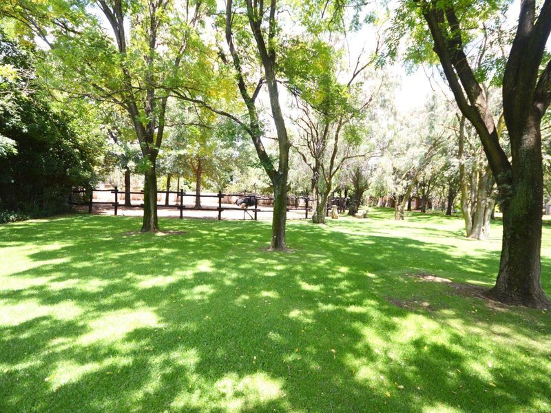 A spacious, well-maintained garden area featuring mature trees and post and rail fencing, providing a serene and private outdoor setting.