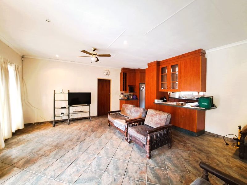 Open-plan living area featuring tiled flooring, a ceiling fan, and a functional kitchen with built-in wooden cabinetry and a breakfast counter.