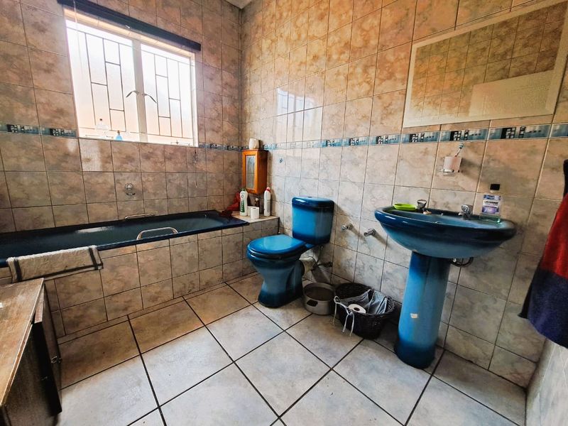 A dated bathroom featuring blue sanitaryware, tiled walls and flooring, and a window with security bars.