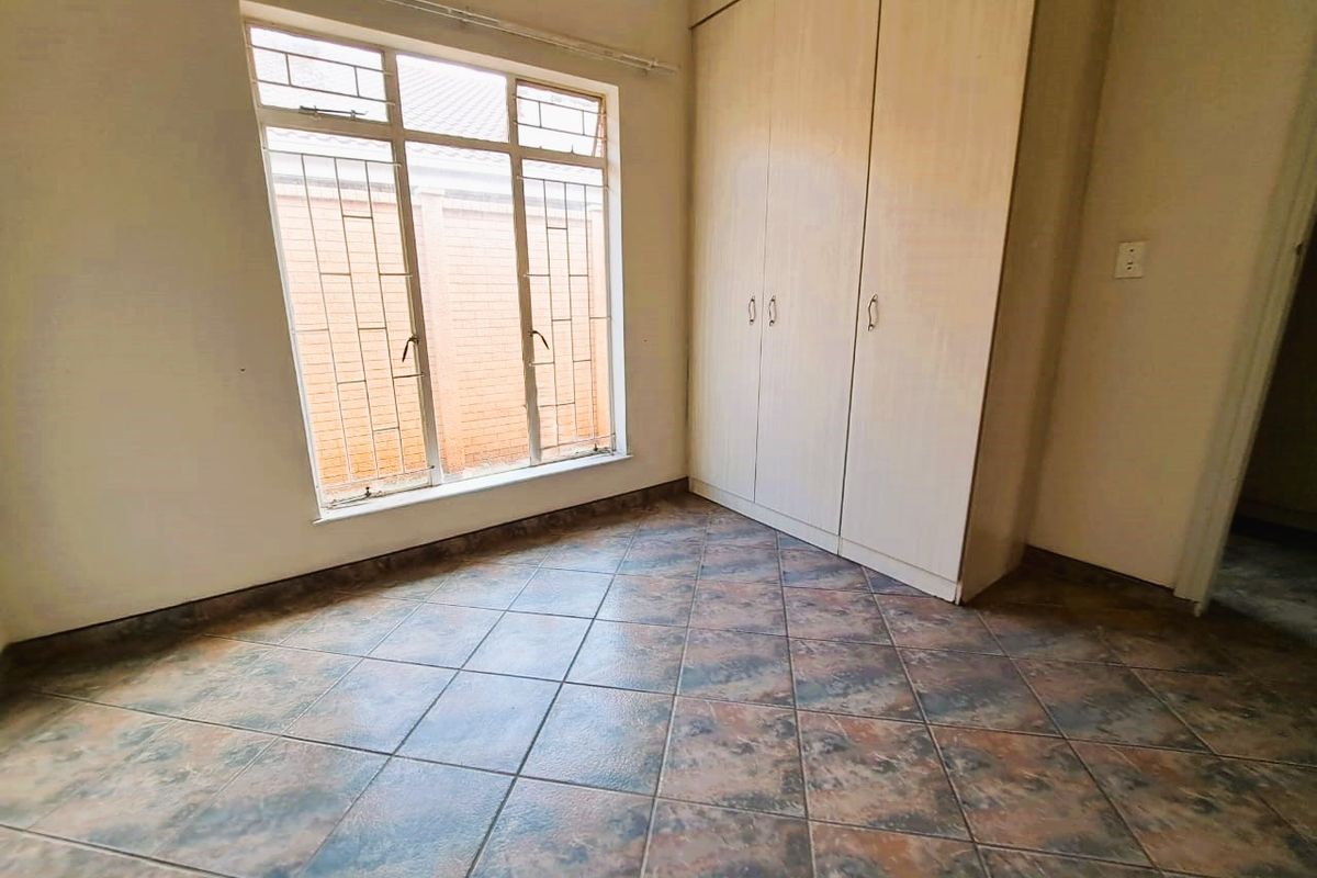 A vacant bedroom featuring built-in cupboards, tiled flooring, and a large window with security bars, offering a blank canvas for personalization.