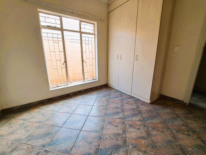 A vacant bedroom featuring built-in cupboards, tiled flooring, and a large window with security bars, offering a blank canvas for personalization.