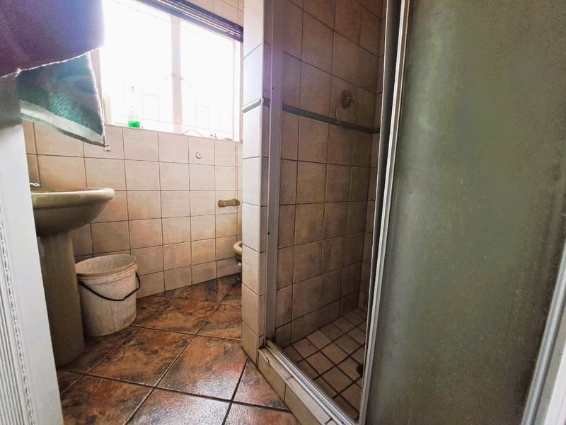 A dated bathroom featuring a shower enclosure, pedestal basin, and toilet with ceramic tiling throughout.