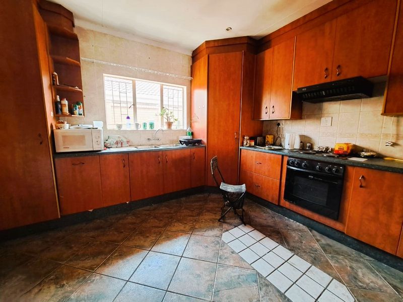 A functional kitchen featuring wooden cabinetry, built-in oven and hob, tiled backsplash, and a double basin sink with security bars on the window.