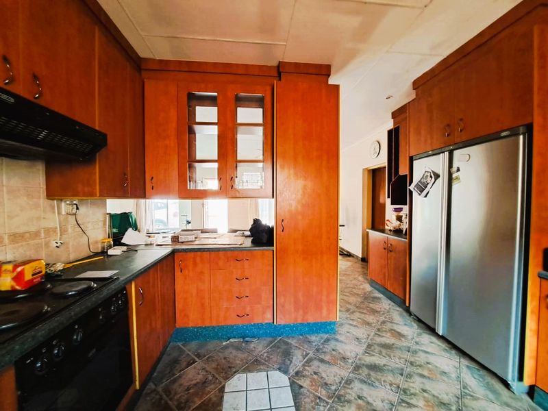 A dated kitchen featuring wooden cabinetry, laminate countertops, and tiled flooring, offering a functional layout with potential for modern renovation.