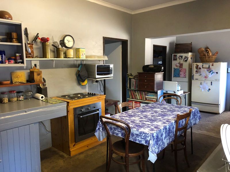 A functional kitchen area featuring built-in oven and hob, wall shelving, and an adjacent dining space with a casual layout.