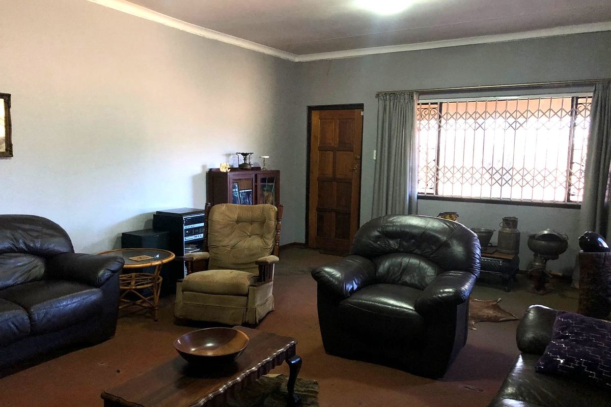 A spacious living room featuring a large window with security gate, coved ceilings, and a solid timber door.