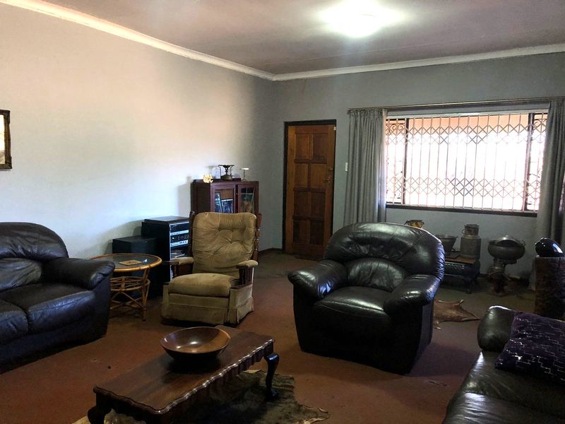 A spacious living room featuring a large window with security gate, coved ceilings, and a solid timber door.