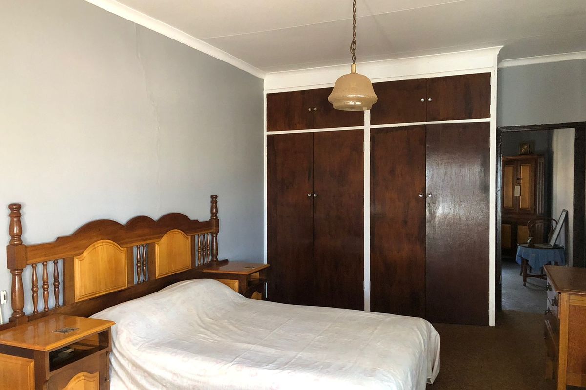 A bedroom featuring built-in wooden cupboards, a ceiling pendant light, and coving, with a visible crack on the wall.